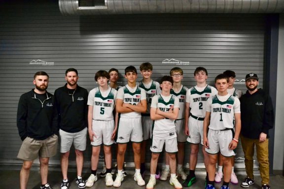 A basketball team poses for a photo with coaches, wearing uniforms and smiles.